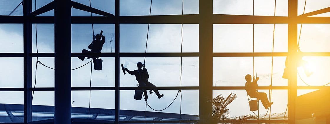 3 window cleaners hanging from harnesses cleaning windows.