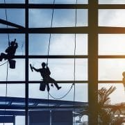 3 window cleaners hanging from harnesses cleaning windows.