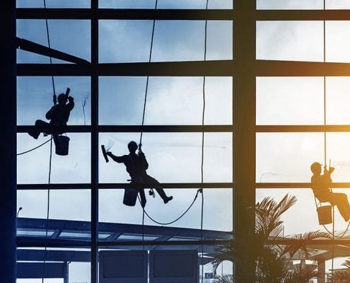 3 window cleaners hanging from harnesses cleaning windows.
