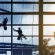 3 window cleaners hanging from harnesses cleaning windows.