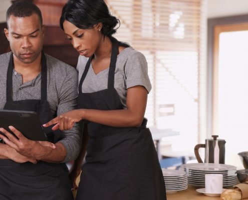 Two people in aprons looking at a tablet.
