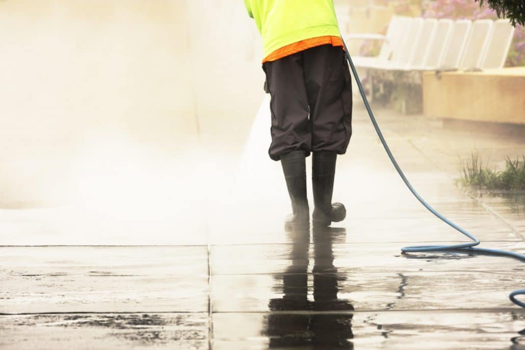 pressure washing second City worker using pressure washer on sidewalk.