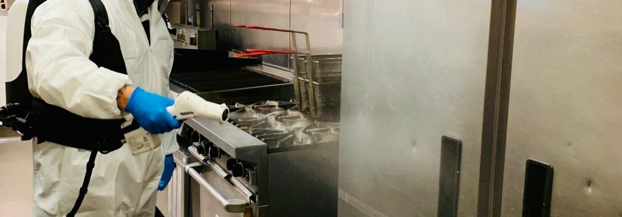 Man in protective suit cleaning and disinfecting a kitchen.