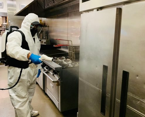 Man in protective suit cleaning and disinfecting a kitchen.