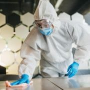 Man in protective suit cleaning and disinfecting table.
