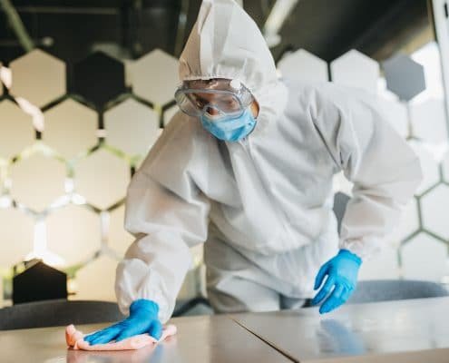 Man in protective suit cleaning and disinfecting table.